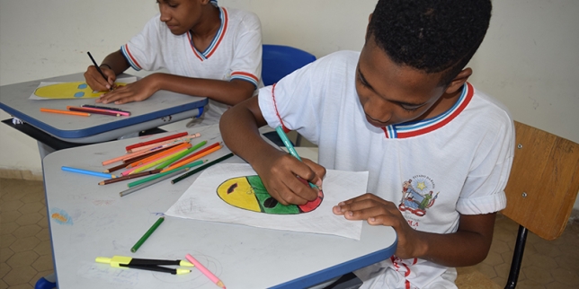 Estudante sentado em sala de aula desenhando em folha de papel com lápis coloridos